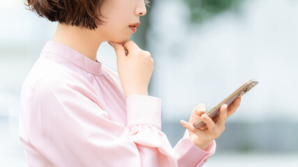 スマートフォンを使いながら考える女性・ビジネスウーマン, Businesswoman Thinking While Using a Smartphone © Trickster*