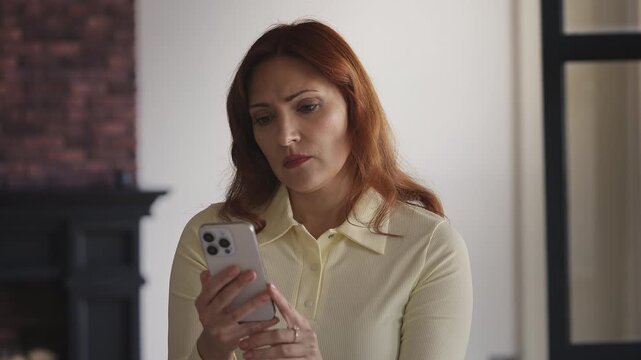 Red-haired woman reading a bad news text on her phone, feeling stressed