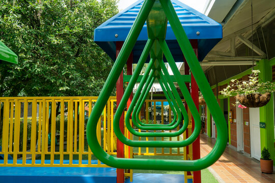 Perspective view through green triangular monkey bars on a colorful children playground structure with blue roofs and yellow fences outdoors.
