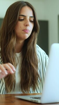 Young focused woman with long hair diligently typing on her laptop, concentrated on her work in a home office setting, demonstrating modern remote work and digital entrepreneurship concepts