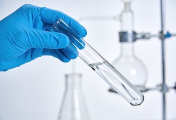 Fototapeta premium Gloved hand holding a clear test tube with liquid in a laboratory setting