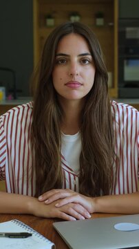 Pensive young brunette woman sitting at a desk with her laptop and notebook, looking away while contemplating or daydreaming, her expression shifting from serious to thoughtful