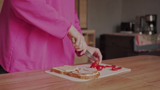 A housewife slices tomatoes to make sandwiches. Delicious breakfast at home.