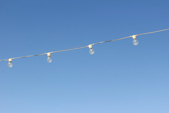 Outdoor String Lights Hanging Against Clear Blue Sky. Festive Patio Bulbs with Copy Space. Minimal Summer Celebration Background. Decorative Garden Lighting for Birthday Party, Wedding Events Decor