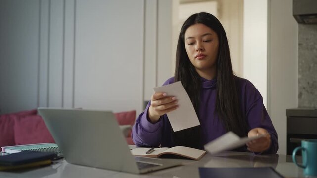 Young Asian woman opening an envelope and reading a letter at home, news
