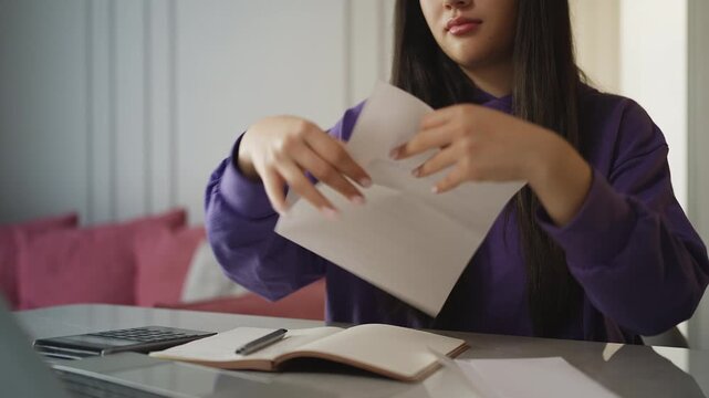 Asian woman in her 20s opening an envelope and reading a notification letter