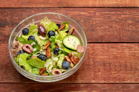 Healthy vegetable salad with romaine, olives, blueberry, cuccumber and walnuts on a rustic, weathered, barn wood table