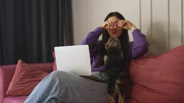 Young Asian woman playing with her dog while typing on a laptop, work break