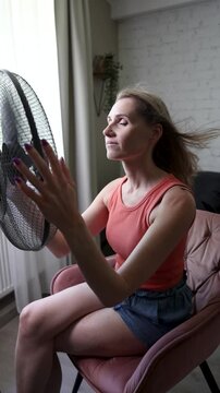Woman enjoying wind from electric fan. Hair is blowing. Air conditioning and cooling at home on summer heat
