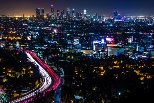 View of the illuminated Los Angeles skyline at night with vibrant light trails from traffic on the highway and glowing city lights Los Angeles, California, United States.