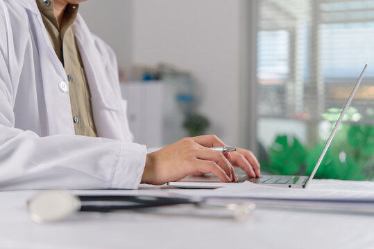 Close up of physician hands using computer keyboard for telemedicine. Healthcare worker in white coat doing medical administration and digital patient records at hospital office desk.