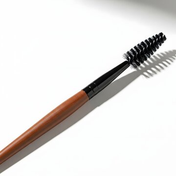 Single spoolie brush with wooden handle against stark white background during studio lighting with soft shadow
