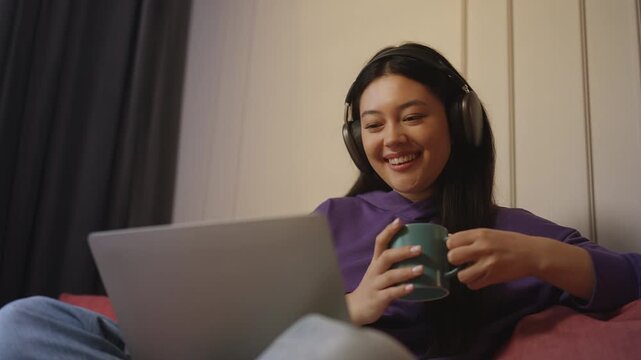 Young Korean woman wearing headphones while watching funny videos on a laptop