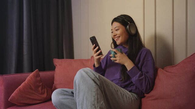 Young Asian woman listening to music in headphones while texting on her phone