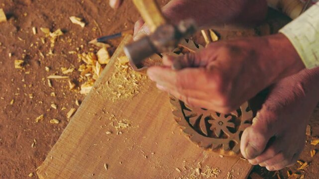 Woodcarver chiseling floral ornament on wooden surface in workshop setting