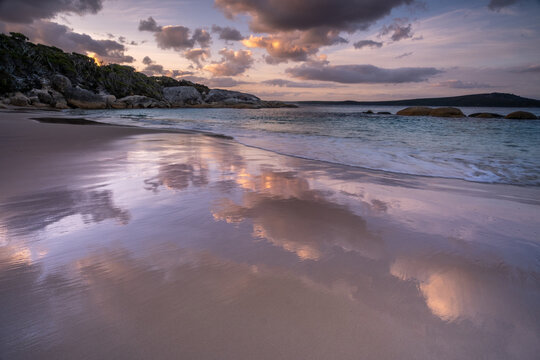 View of Waterfall Beach with wet sand reflecting the soft sunset clouds and gentle waves washing onto the shore in Albany, WA, Australia.