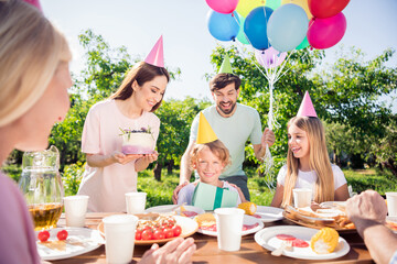 Fototapeta premium Family celebrating a child's birthday outdoors with cake, balloons and gifts at a sunny backyard picnic party with parents and siblings