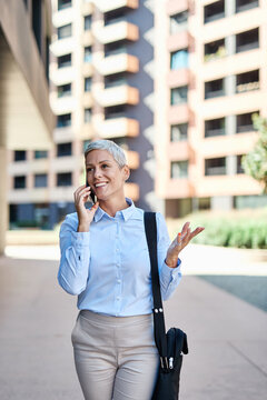 Portrait of a young businesswoman woman using a smartphone mobile phone walking down the street, surrounded by moder corporate office buildings
