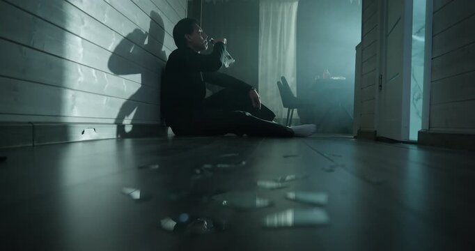 Depressed drunk man sit floor dark room drink alcohol bottle. Sad male suffer alco addiction, loneliness. Social problem, crisis, mental health struggle concept. Alcoholic guy feel grief, anxiety doom