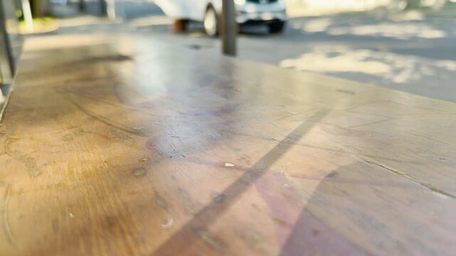 A wooden bench rests quietly at a sunlit public transport stop in Simferopol, Crimea. The empty seat creates a lonely yet peaceful feeling of waiting.