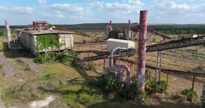 Old phosphate processing plant in central Florida with weathered structure, conveyor belts and overgrown vegetation.