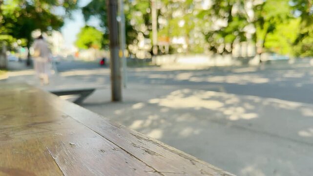 An empty wooden bench sits at a sunny bus stop as a person walks away in Simferopol, Crimea. This quiet scene brings a lonely, nostalgic, and peaceful feeling.