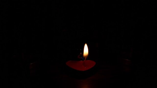 Multiple small red heart-shaped tealight candles sequentially ignite on dark wooden surface, growing from one flame to a full glowing group in complete darkness.