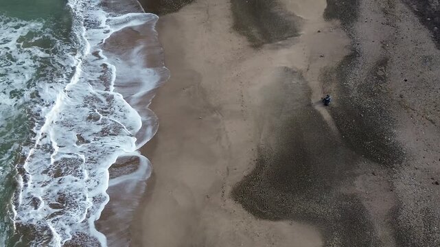 Sandy beach waves under clear blue sky, cinematic aerial drone footage of ocean coastline, harbor, moving traffic, trees and coastal urban landscape. scenic view of port area and waterfront road.