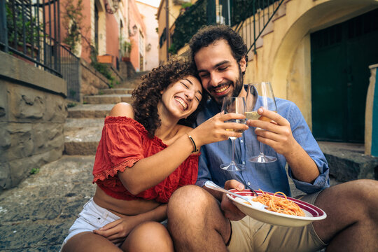 Happy young couple toasting with wine while enjoying pasta on historic Italian steps