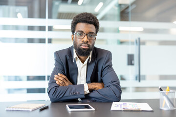 Confident business person sitting formally at a modern office desk, wearing glasses and a suit,...