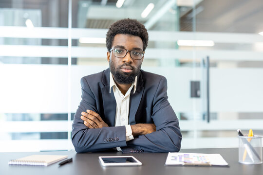 Confident business person sitting formally at a modern office desk, wearing glasses and a suit, displaying professionalism and serious focus during a corporate meeting or interview