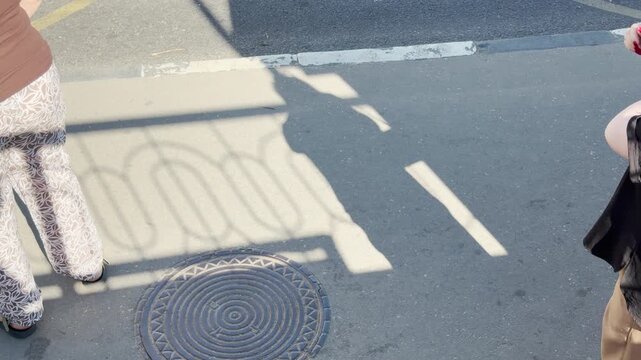 Patient passengers wait calmly at a sunny bus stop in Simferopol, Crimea. The geometric shadows on the pavement create a peaceful and expectant atmosphere during the warm morning.