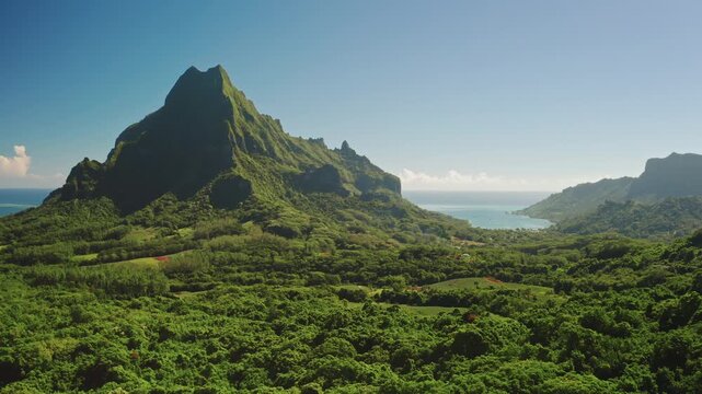 Aerial view drone flight over lush green tropical island featuring towering mountains peak, dense jungle foliage, and scenic bays, highlighting the natural beauty of French Polynesia landscape