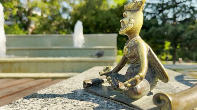A serene bee figurine sits in a yoga pose on a stone ledge in a park in Simferopol, Crimea. The cute statue inspires a peaceful sense of calm relaxation. A sunny fountain flows behind it.