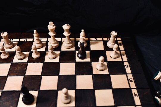Horizontal close-up of a chess game in progress on a wooden board against a black background