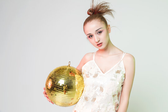 Young woman holding gold disco ball in stylish party pose