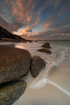 View of large granite boulders on the white sand beach of Frenchman Bay at sunset with soft waves washing over the shore in Frenchman Bay, Western Australia, Australia.