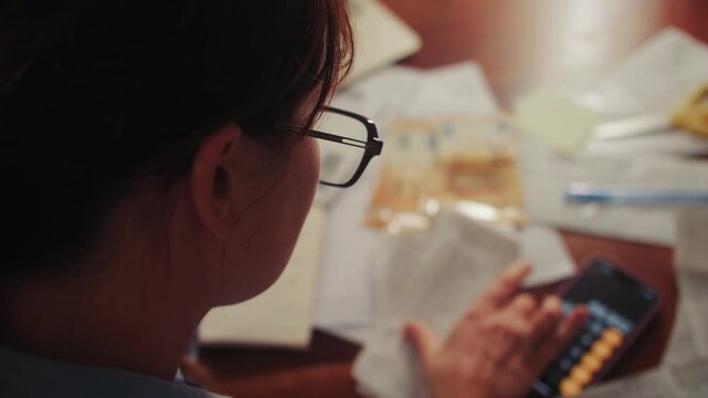 A woman calculates monthly expenses, for a period going through her purchase receipts and adding up on a calculator. Concept of a family budget. High quality 4k footage