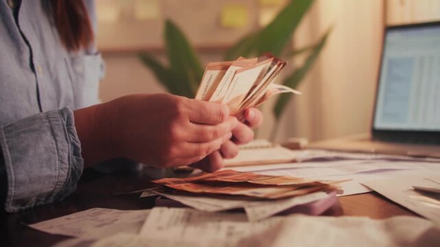 Close up of hands counting euros while sitting at a table. Utility bills and receipts are on the table. The process of calculating a family budget. High quality 4k footage