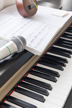 The close-up image shows a microphone placed on a piano with sheet music open above, suggesting a music practice, singing, or performance in a studio or home.