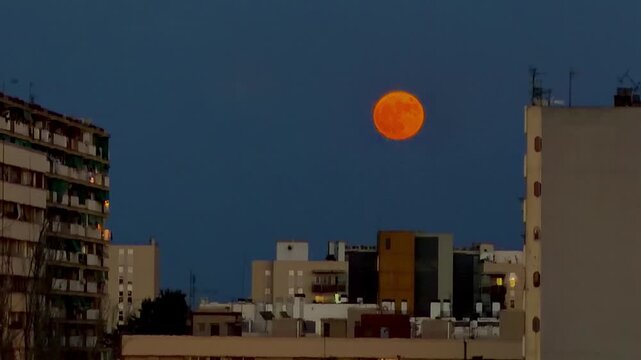 huge full moon of orange color rising over the night city and residential buildings