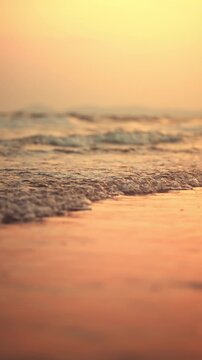 Close-up of gentle sea waves washing onto a sandy beach during golden hour sunset. Beautiful low-angle view with shallow depth of field, Peaceful mood of a summer vacation at the tropical shore.