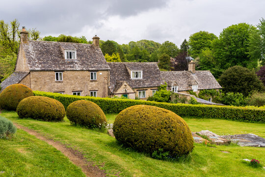 Charming stone cottages with traditional architecture, lush green gardens and topiary in the historic Cotswolds.
