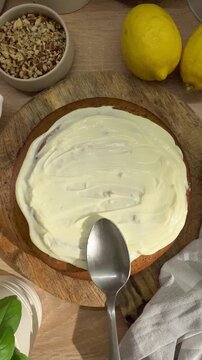 Person spreading white cream frosting on homemade cake