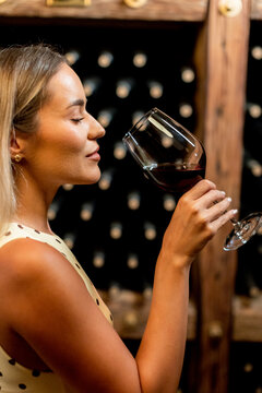 Woman enjoys red wine in a wine cellar while savoring the aroma of the drink