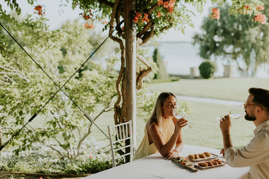 Couple enjoys drinks and food at outdoor table near lake during sunny day