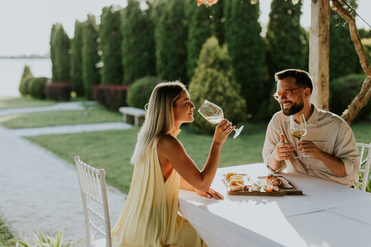 Couple enjoys dinner with wine by the water at sunset during a warm evening