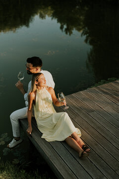 Couple relaxes on dock by water while enjoying drinks during sunset