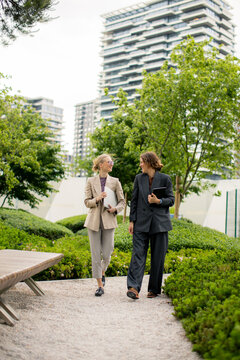 Business women walking in urban park with green plants in daytime