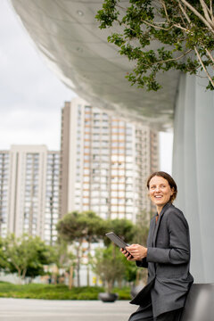 Woman sitting outside using tablet with modern buildings in the background during the day